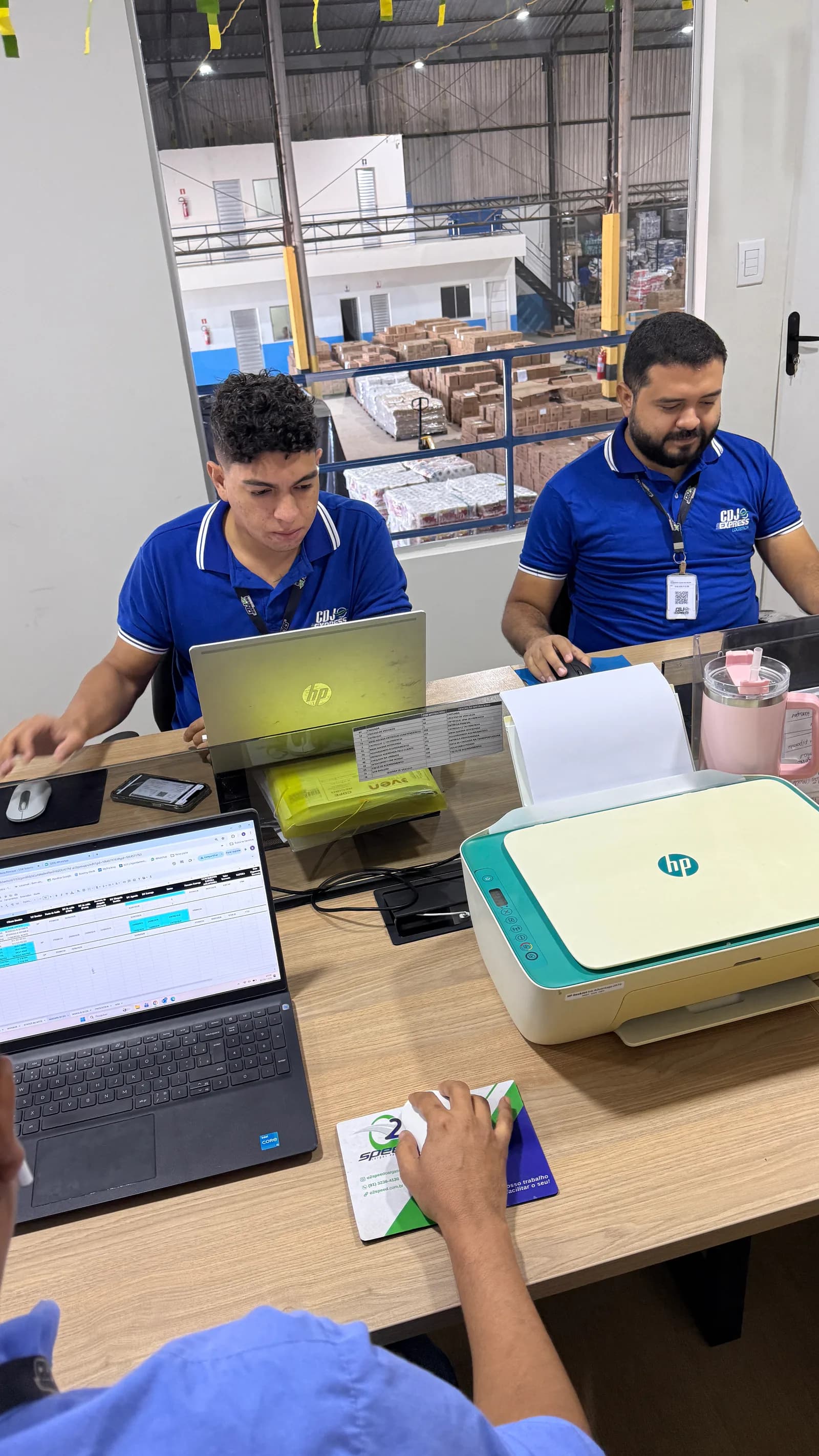 Profissionais da CDJ Express trabalhando com computadores diante do galpão